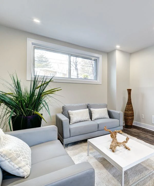 A modern basement remodeling project in Oswego, IL featuring a grey sofa, white coffee table, and large window for natural light.