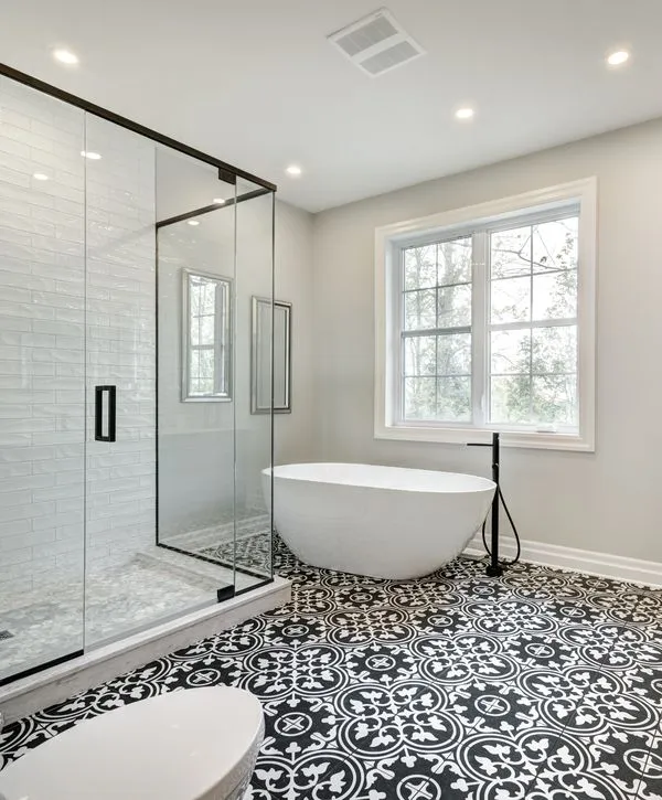 Luxury bathroom remodeling in Oswego, IL featuring a white freestanding bathtub, glass walk-in shower, and black and white patterned floor tile.