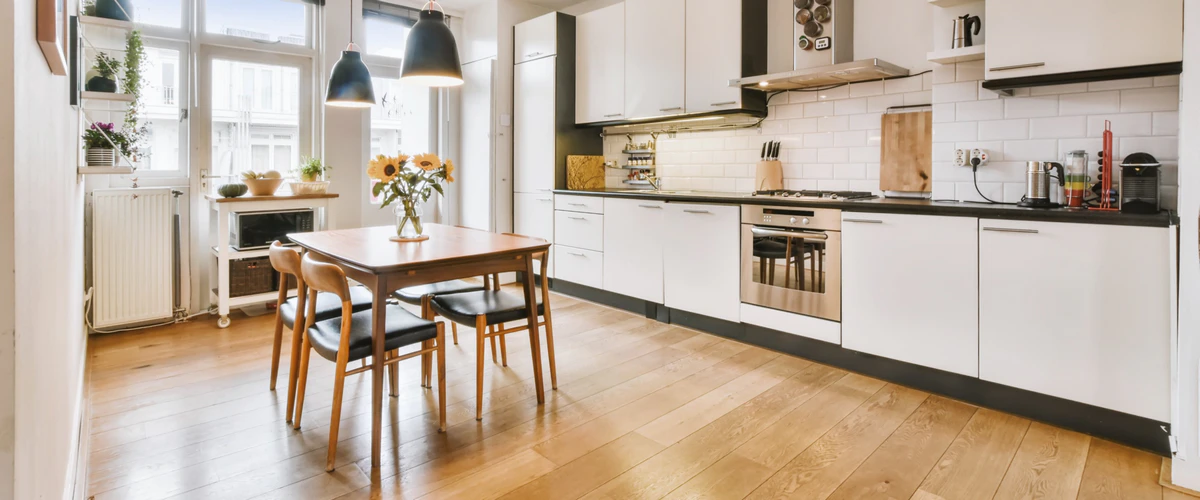 A bright Scandinavian-inspired kitchen with white cabinetry, light wood floors, and a wooden dining table topped with fresh sunflowers.