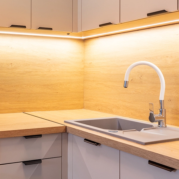 Modern kitchen corner with wood backsplash, under-cabinet lighting, and white faucet.