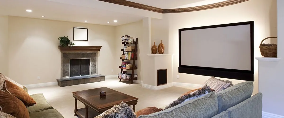 A professionally finished basement featuring a large home theater projection screen, cozy stone fireplace, and comfortable sectional seating.
