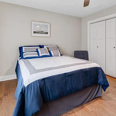 Bedroom with blue and gray bedding, hardwood floors, framed wall art above the bed, and a white closet door.