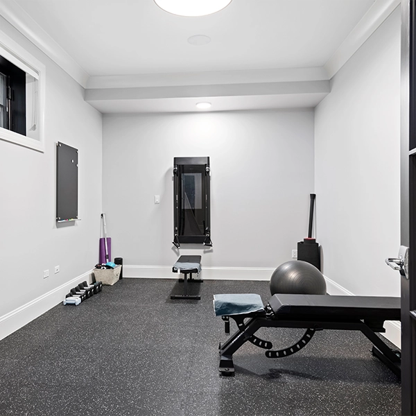 Home gym with weight bench, exercise equipment, and rubber flooring.