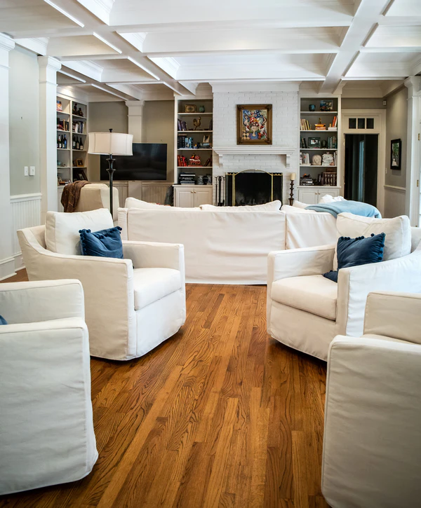 A spacious and modern living room featuring white sofas, dark blue pillows, and a brick fireplace, part of professional home additions in Yorkville, IL.