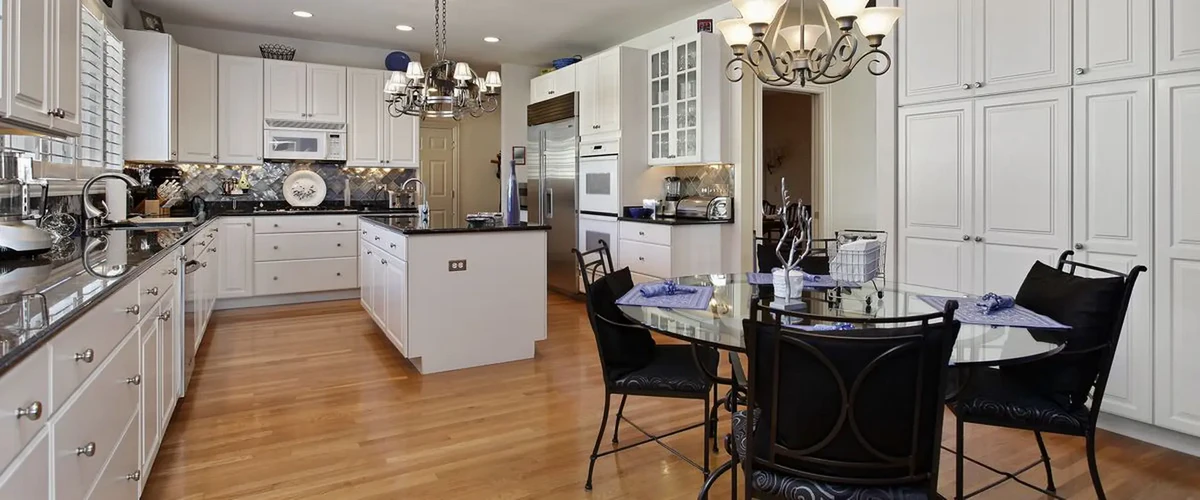 Open concept kitchen with white cabinetry, stainless steel refrigerator, and a circular glass dining table with black chairs.