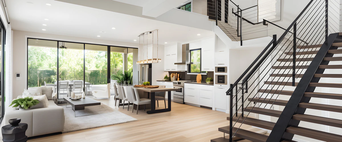 A spacious open-concept home interior with a modern kitchen, dining area, and living room featuring large windows.