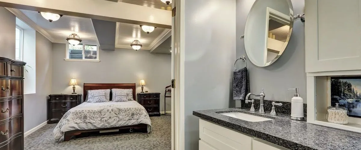 Interior view of a renovated basement bedroom featuring a dark wood bed frame and a luxury bathroom vanity with granite countertops.