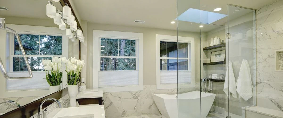 Spacious master bathroom featuring marble wall tiles, a large skylight for natural light, a white freestanding bathtub, and a glass shower enclosure.