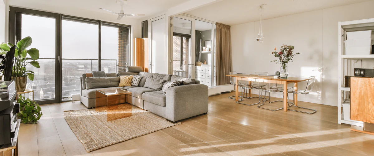 Spacious open-concept living room featuring a large gray sectional sofa, jute rug, and a wooden dining table under a ceiling fan.
