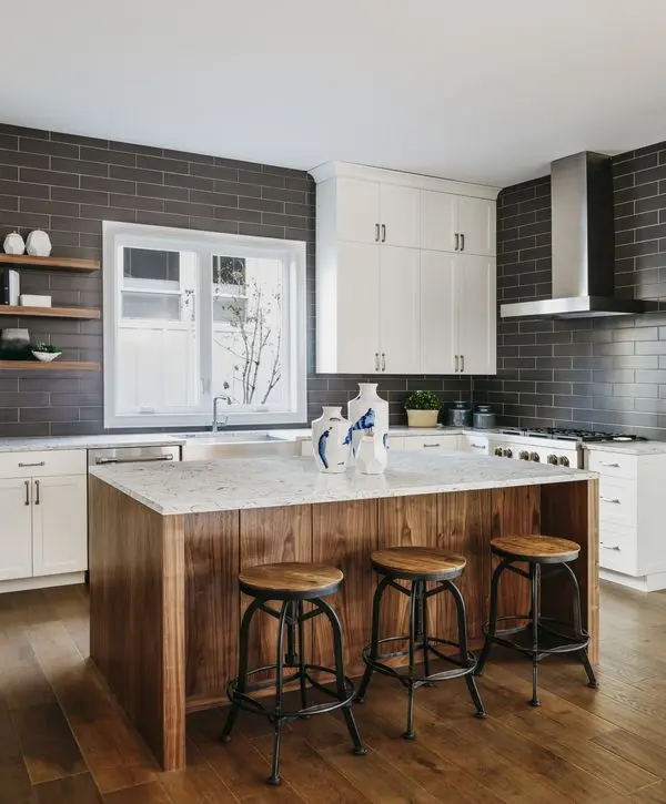 A modern kitchen renovation by kitchen remodeling companies in Yorkville, IL, featuring dark gray subway tile, white upper cabinets, and a large wood-paneled island with industrial bar stools.