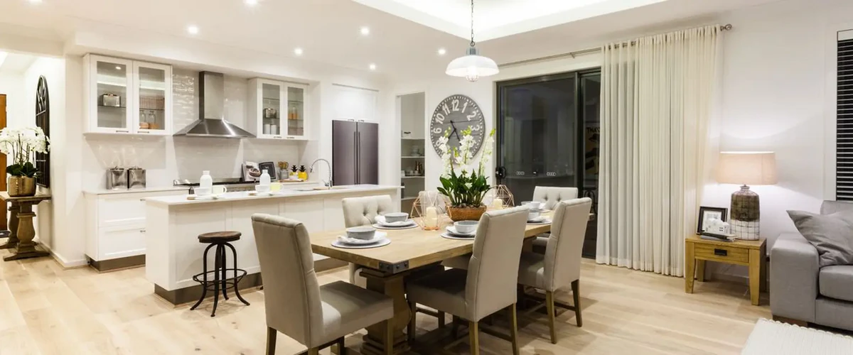 A bright, open-concept kitchen and dining area featuring white shaker cabinets, a stainless steel range hood, and a large wooden dining table set for a family meal.