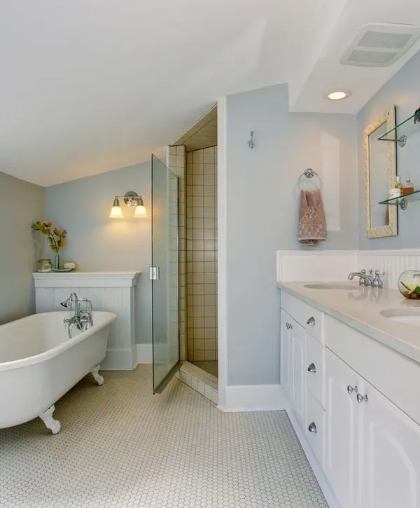 A master bathroom in Yorkville, IL renovated by bathroom remodeling companies, featuring a classic white clawfoot tub, a glass-door walk-in shower, and a white double vanity against light blue walls.