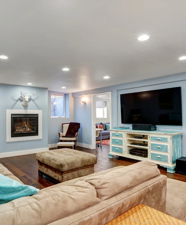 Cozy completed basement renovation in Yorkville, IL featuring a fireplace, beige sectional, and a large TV on a rustic blue media console.